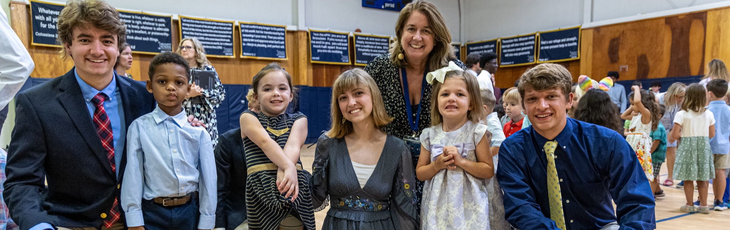 Three teachers with young students in a school gymnasium smiling at the camera